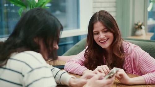 Two Young Women Discussing Smartphone at Table