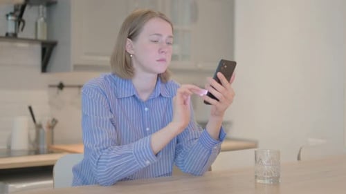 Woman Uses Phone Sitting at Kitchen Table