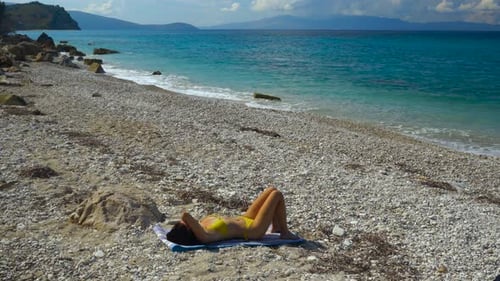Girl in swimsuit sunbathe alone on peaceful beach with pebbles washed by blue turquoise sea on summe