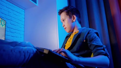 Teenager playing video game on PC. Boy plays computer games using keyboard while sitting at home.