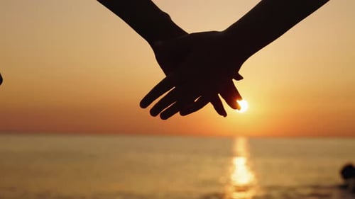 Hands of Mother and Daughter Joining Together Against Sunrise Over Calm Sea
