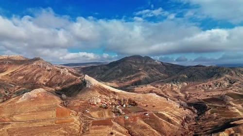 Aerial View of Rugged Mountains and Rural Valley Under Dramatic Clouds
