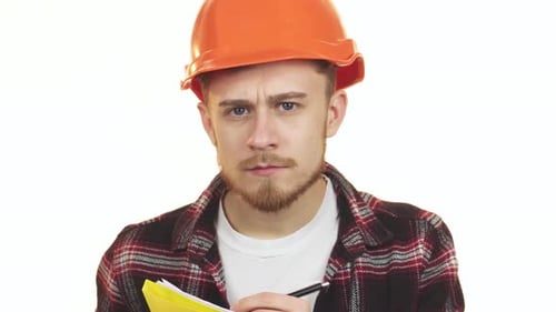 Focused Young Male Architect in an Orange Hardhat Diligently Taking Notes