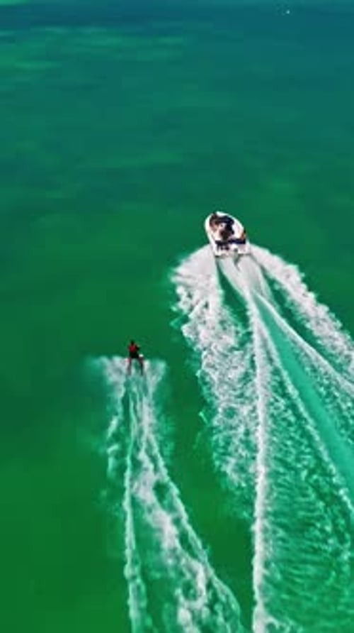 A Drone View of a Guy Skiing Behind a Speedboat on Crystalclear Water Extreme Sports Recreational
