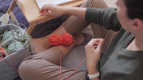 Woman Sits Indoors Crocheting Ball of Yarn