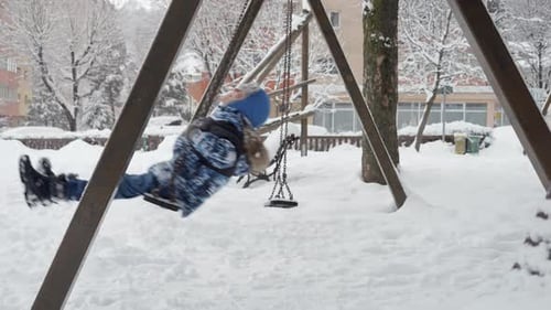 Slow motion footage of a happy toddler boy enjoying a swing ride in a snowy playground