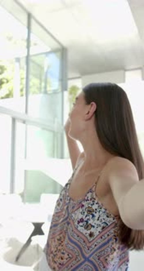 Vidéo verticale : adolescente souriante à la maison, prenant un selfie dans un salon lumineux et moderne