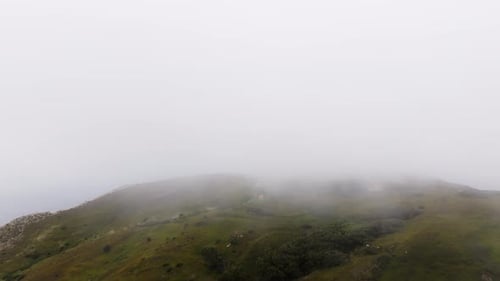 Fog Enveloping the Lush Green Summit of a Mountain