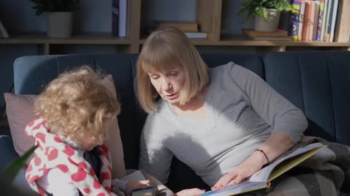 Grandmother and Child Reading a Book Together on Couch