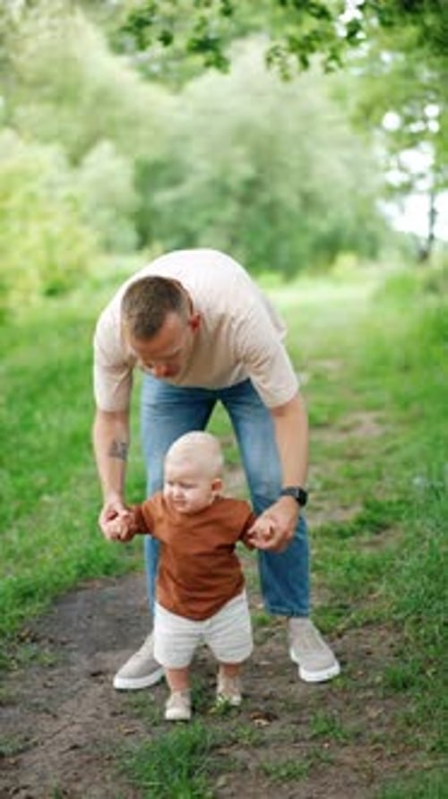 Caucasian dad leads his cute son by the alley in the park.
