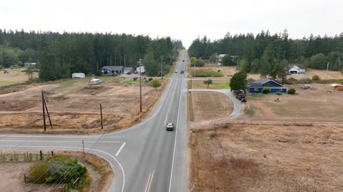 Drone shot tracking a car driving down a rural highway on Whidbey Island.