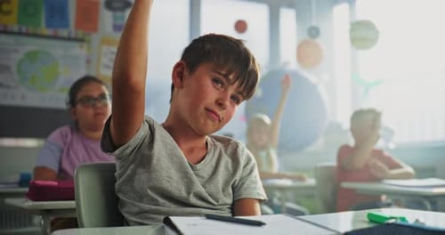 Primary School Boy Sitting at Desk Raising Hand and Giving Correct Answer on Teacher's Question