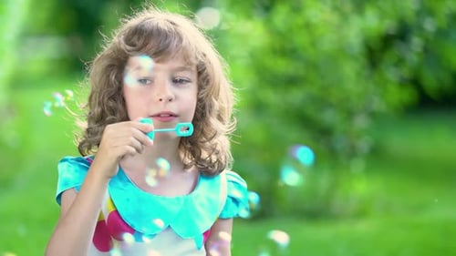 A happy child blows soap bubbles in a summer park. Slow motion