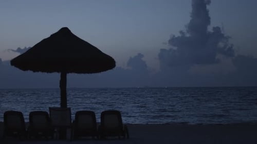 Beach chairs and straw umbrella on seashore at dusk. Static