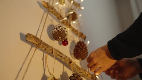 A young woman hangs Christmas decoration on the wall, lanterns and branches with ornaments.
