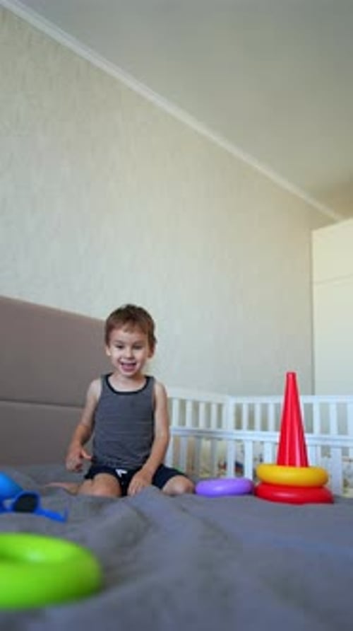 Un niño sonriente sentado en la cama grande juega con la pirámide.