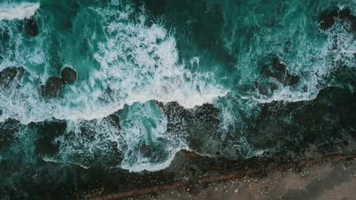 Luftaufnahme der dunklen blaugrünen Meereswellen von Wasser, das auf Felsen zusammenprallt
