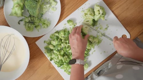 Woman chopping broccoli on a cutting board for a quiche recipe, top view
