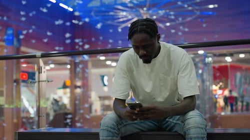Hombre famoso sentado en el interior usando el teléfono en un colorido centro comercial