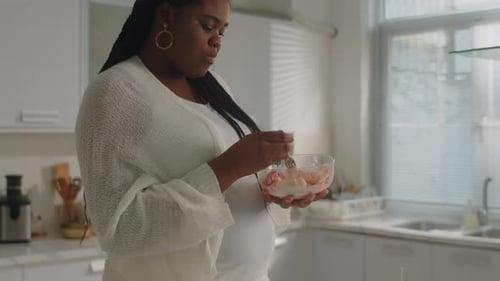 Pregnant Woman Enjoys Fruit Bowl in Bright Kitchen