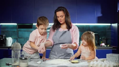 Caucasian Son and Daughter Help Their Mother Beat an Egg Into Flour