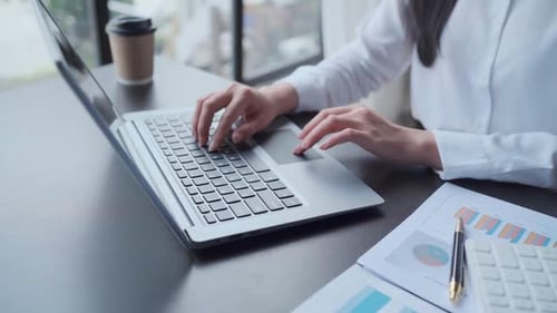 Woman Typing on Laptop in Office with Data Charts