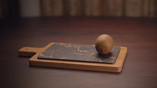 Hand Places Three Kiwis on a Cutting Board