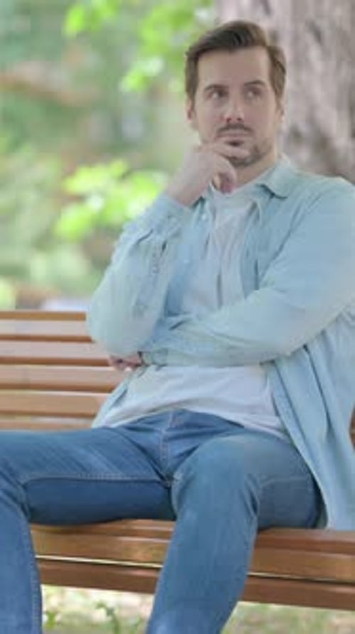 Man Thoughtfully Sitting on Park Bench in Sunlight
