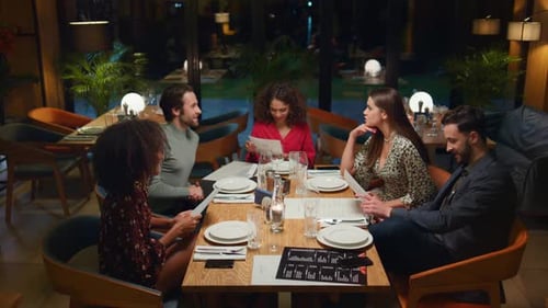 Friends Talking Chatting Together In Fancy Restaurant. Young People Look Menu At Cafe Table. Chee...