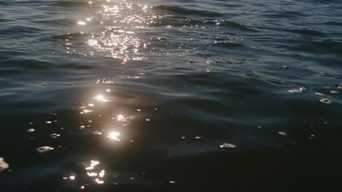 Sunlight reflection glimmering on water during sunset. Gentle waves rolling on a lake.