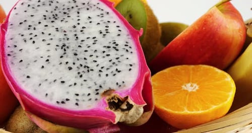 Fruit basket with dragon fruit pitahaya, kiwi, oranges, bananas and apples on a white background.