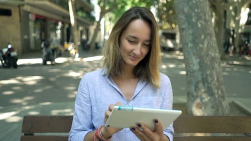 Young businesswoman browsing the web on tablet computer sitting on city bench