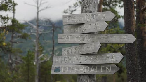 A rustic wooden signpost points in multiple directions, indicating different mountain trails and des