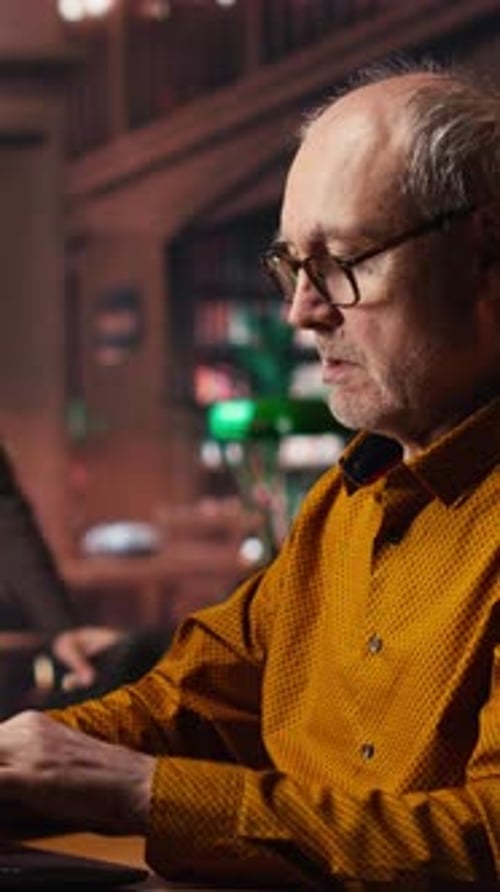 Vertical Video Elderly Male Adult Reviewing Academic Text on a Laptop at the University
