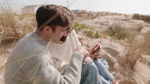Couple Using Smartphone Together on Sandy Beach