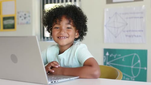 African American male child smiling, engaging with open laptop at school table for learning