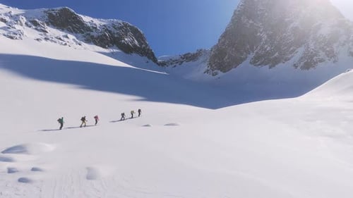 Luftaufnahme, die eine Gruppe von Bergsteigern zeigt, die im Sonnenlicht schneebedeckte Berge hinaufwandern. Cima C
