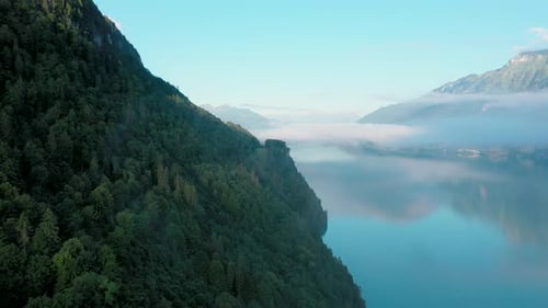 Drone flight over a beautiful Swiss alpine lake. The drone flies above the valley forest to reveal t