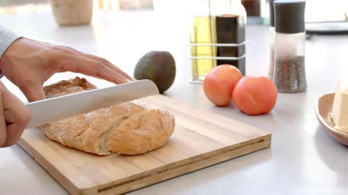 Person Slicing Bread on Cutting Board in Kitchen