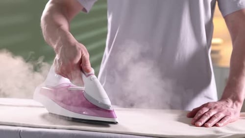 Man ironing pants on board at home, closeup. Slow motion effect