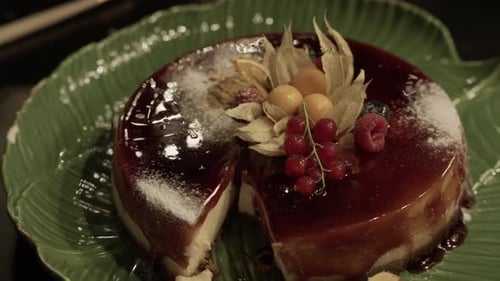 Caramel flan with berries and powdered sugar on green leaf plate