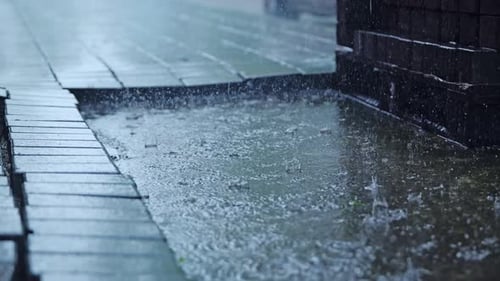 Schwerer Regen fällt in Zeitlupe auf ein Betonfeld zwischen Kopfsteinpflaster in der Stadt