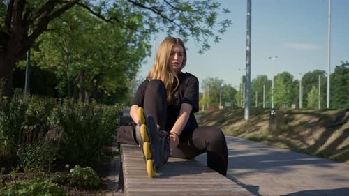 young beautiful girl in park tying laces on roller skates before skating workout active lifestyle
