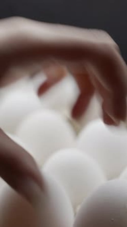 Hand puts eggs in a box. Eggs are stacked in a tray. Vertical video