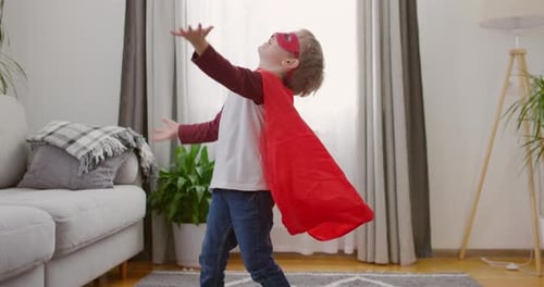 Child in Superhero Costume with Red Cape and Mask Playing with Balloons in Home