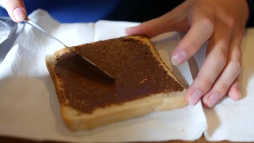 Une tranche de pain blanc tartinée de noisettes à l'aide d'un couteau, les mains tenant