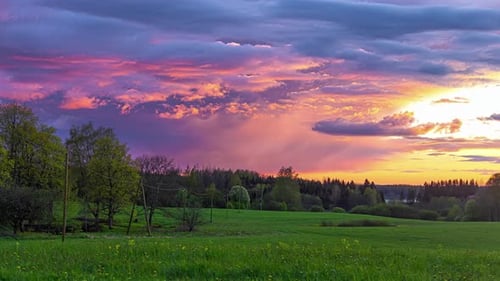 Clouds passing by in timelapse on the sunset sky over a beautiful rural green field landscape with y