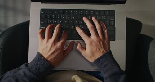 Ansicht von oben auf eine Person mit Laptop, Mann, der einen Computer an seinen Beinen hält und auf einem Stuhl sitzt und tippt