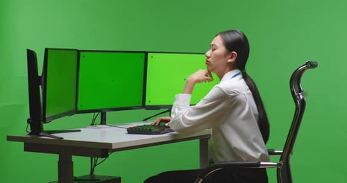 Side View Of Asian Woman Thinking While Working With Mock Up Multiple Monitor In Green Screen Studio