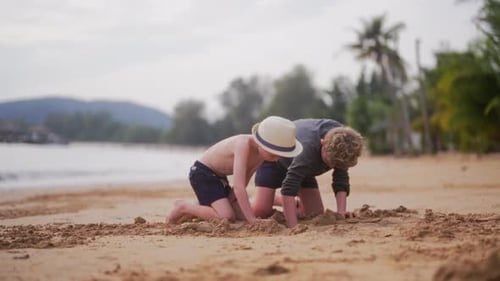 Two Boys Digging In The Sand On A Beach